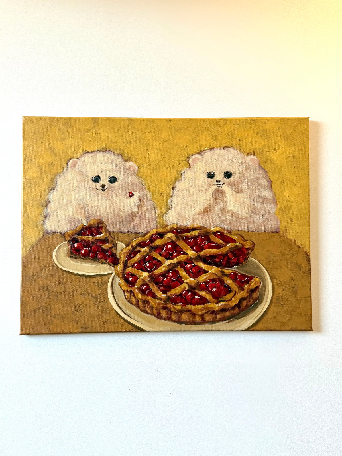 A square canvas painting depicting two fluffy white dogs sitting behind a cherry pie and a slice of pie on plates, set against a textured gold background.
